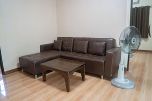 A living room with a brown leather sofa, a wooden coffee table, and a standing fan. - Honey Home Pai (Pai)