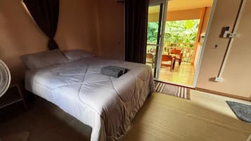 Een slaapkamer met een bed, een ventilator en uitzicht op een buitenruimte met een stoel en een tafel.