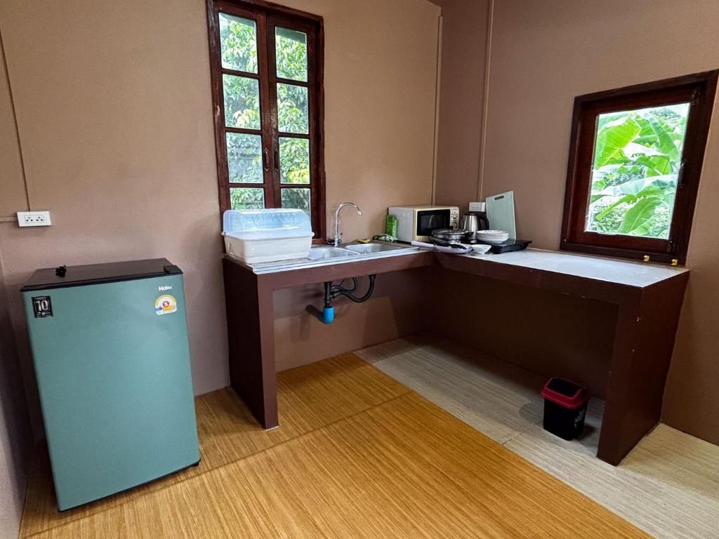 A compact kitchen with a refrigerator, microwave, sink, and window with a view of greenery.