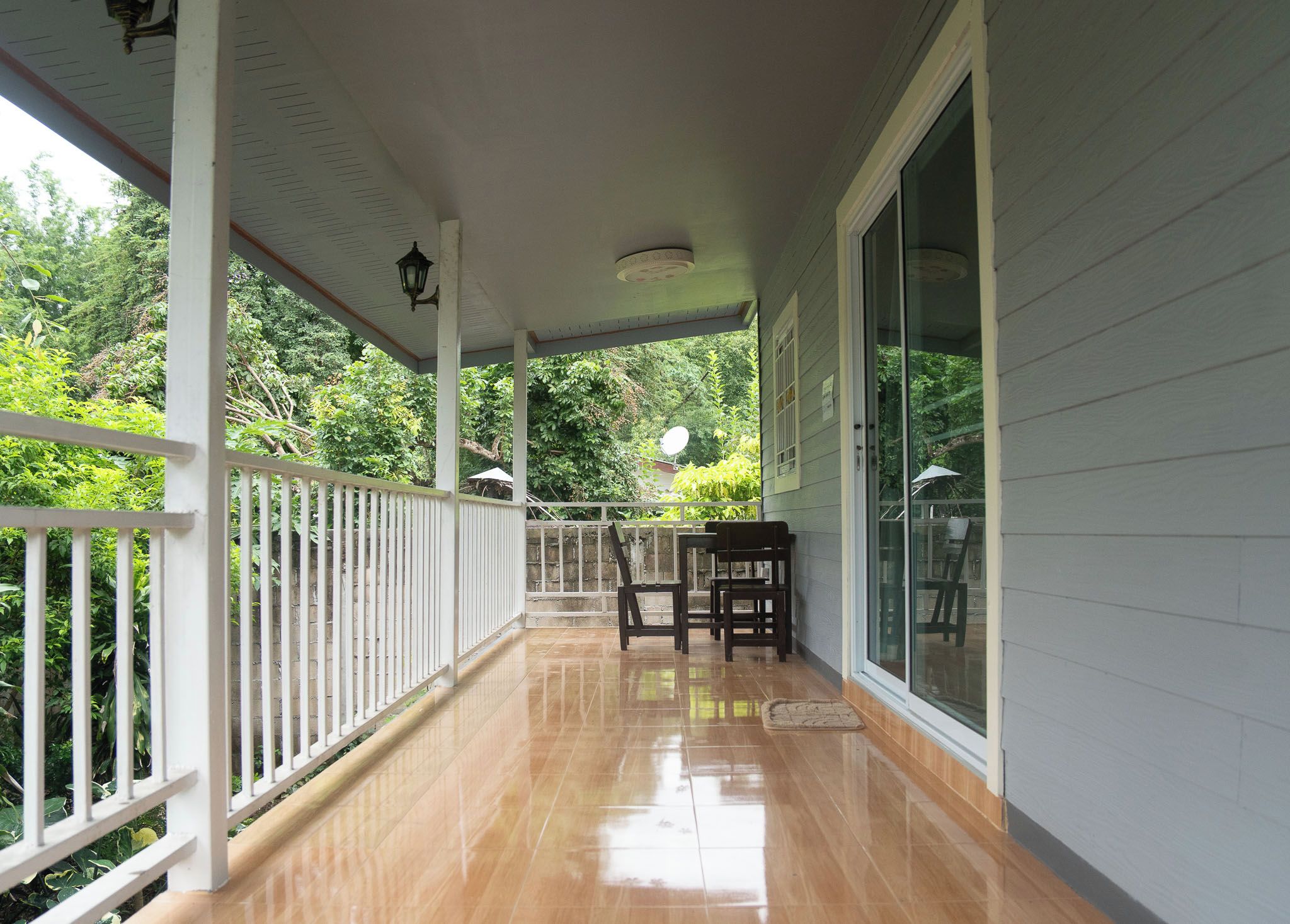 A covered porch with a wooden railing, a table with chairs, and a glass door leading to a garden.