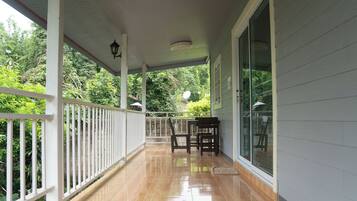 A covered porch with a wooden railing, a table with chairs, and a glass door leading to a garden.