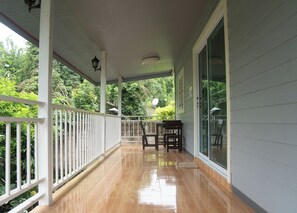 A covered porch with a wooden railing, a table with chairs, and a glass door leading to a garden.