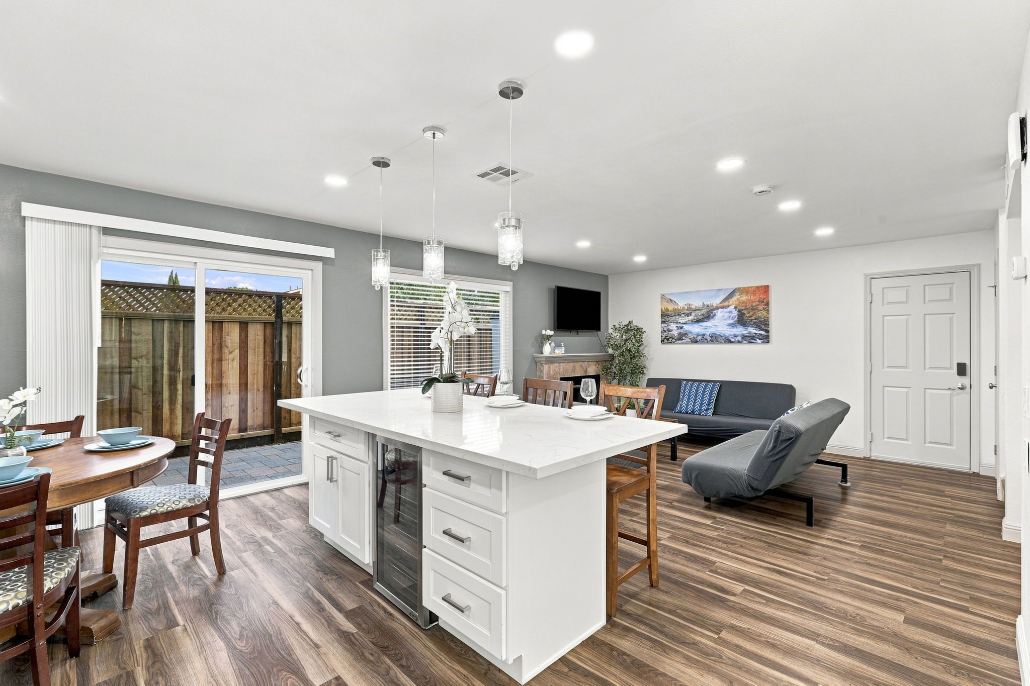 A modern kitchen with a central island, dining area with chairs, and a living room with a sofa.