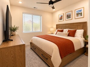 A bedroom with a bed, a television, a ceiling fan, a window with blinds, and framed pictures on the wall. - Terra Summit w/ Rooftop Hot Tub + Lazy River (Hurricane)