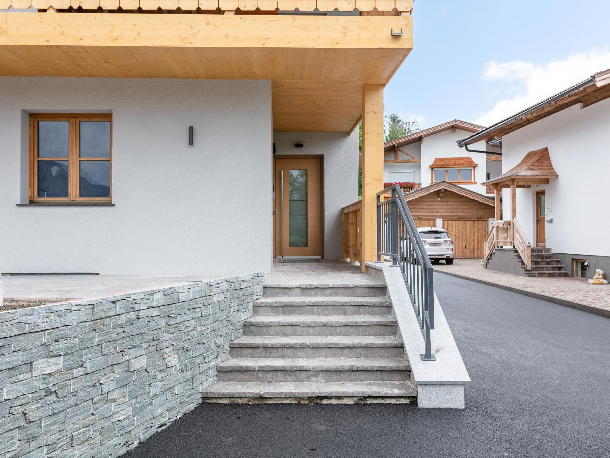 Un bâtiment moderne avec un mur en pierre, un escalier en bois et une voiture garée dans l’allée.