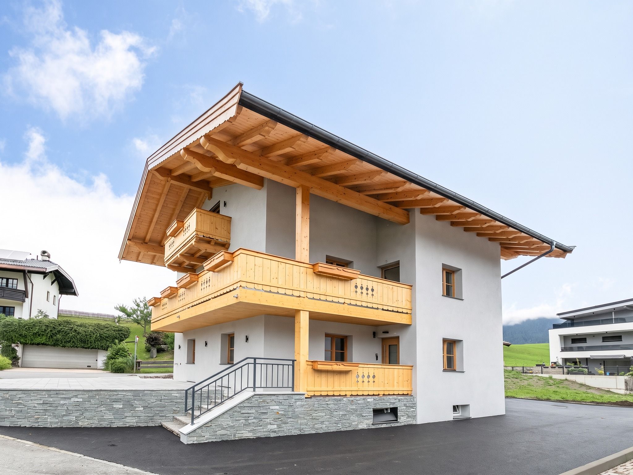 Ein zweigeschossiges Haus mit Balkon, Steinmauer und befestigter Auffahrt.