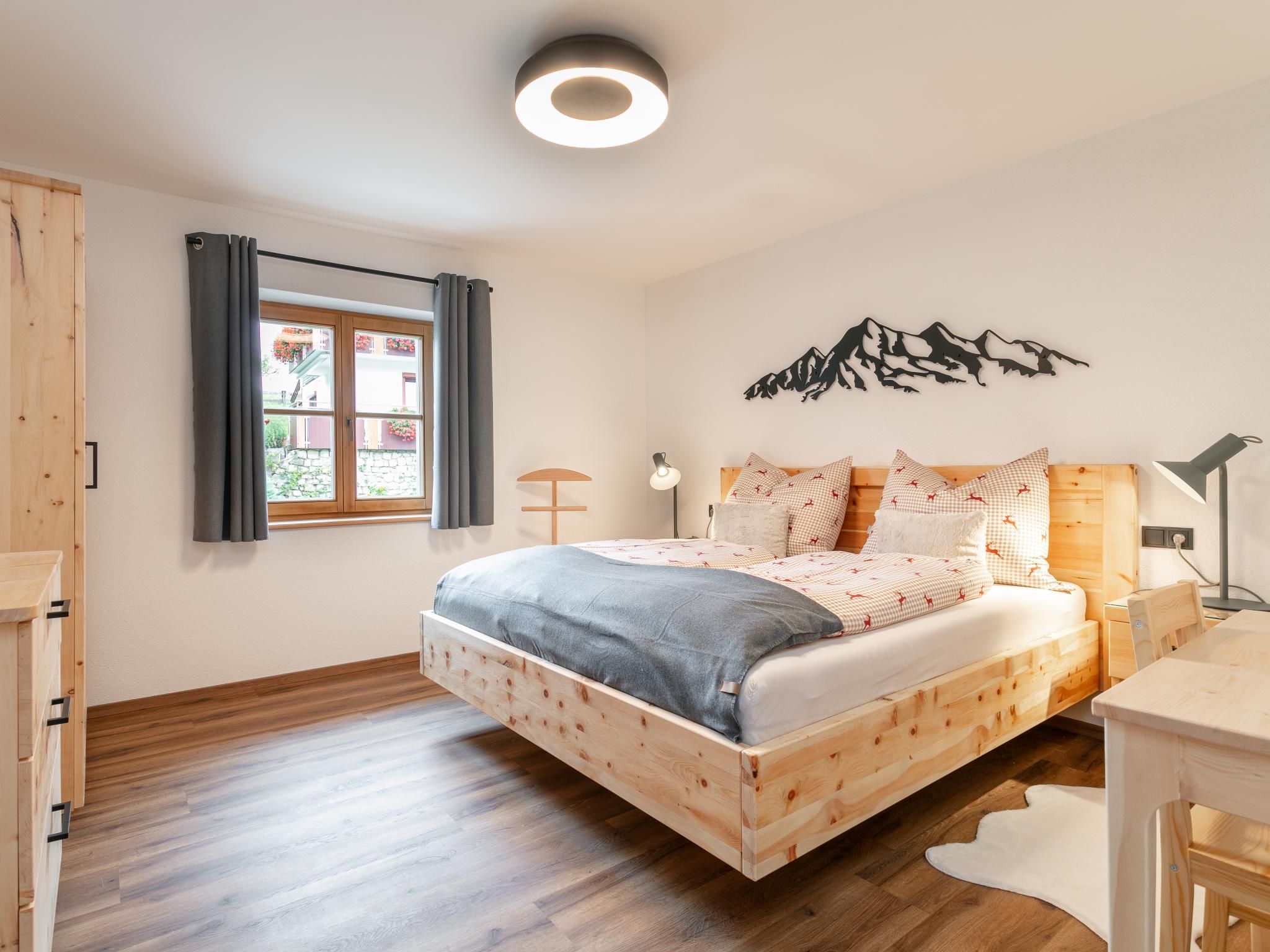 A bedroom with a wooden bed, a window with curtains, a wall-mounted lamp, and a mountain silhouette decoration.