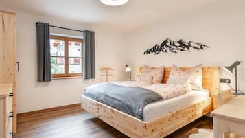 A bedroom with a wooden bed, a window with curtains, a wall-mounted lamp, and a mountain silhouette decoration.