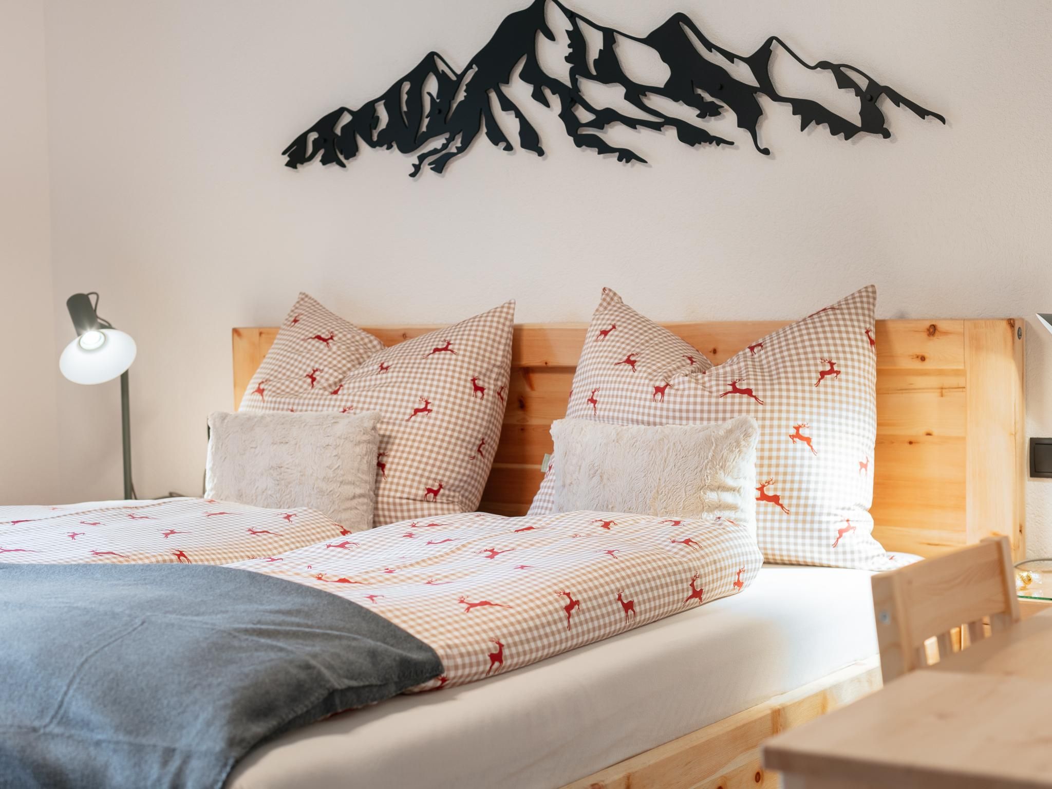 Ein Schlafzimmer mit Bett, Kissen, Decke, einem Wandbild von Bergen, einer Nachttischlampe und einem Holzkopfteil.