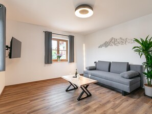 A modern living room with a grey sofa, a wooden coffee table, and a flat-screen TV mounted on the wall.