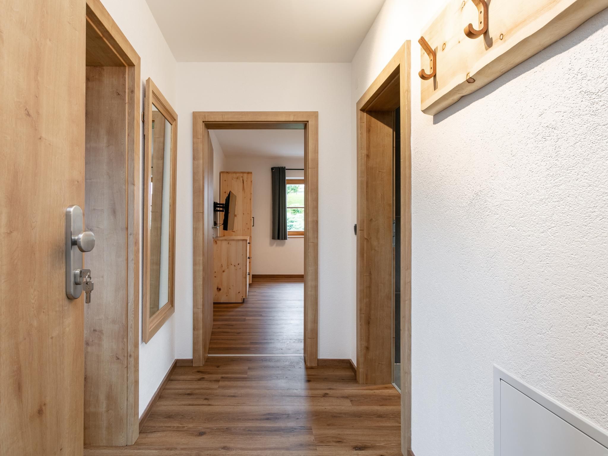 Ein Flur mit Holztüren und Blick in einen Raum mit Fenster und Spiegel.
