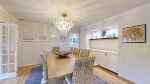 A dining room with a wooden table, wicker chairs, a chandelier, and framed artwork on the walls. - Elegant 5 Bedroom House (Hilton Head)
