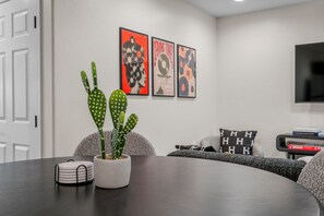 Ein modernes Wohnzimmer mit einem dunklen Holztisch, einem Kübelkaktus und einem wandmontierten Flachbildfernseher.
