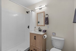 Een badkamer met een douche, wastafel, toilet en spiegel.