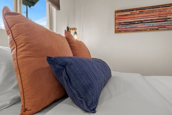 Ein Bett mit zwei Kissen, einem orangen und einem blauen, in einem Zimmer mit Wandbild.