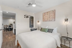 A bedroom with a large bed, a ceiling fan, a wall-mounted guitar display, and a small table with a lamp. - The Rialto at Hoff & Co | Off 4th Ave (Tucson)