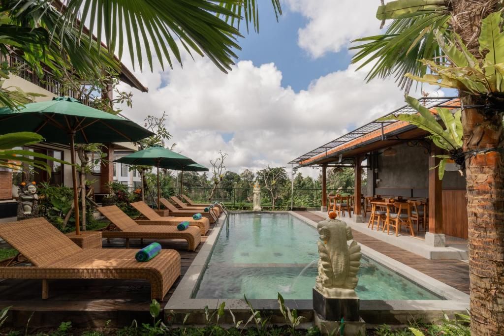Un área de piscina con sillones de playa y sombrillas, rodeada de vegetación y un cielo despejado.