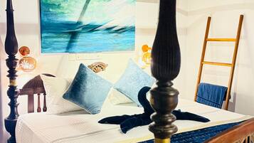A four-poster bed with a wooden headboard, a blue bedspread, and a painting of a seascape on the wall.