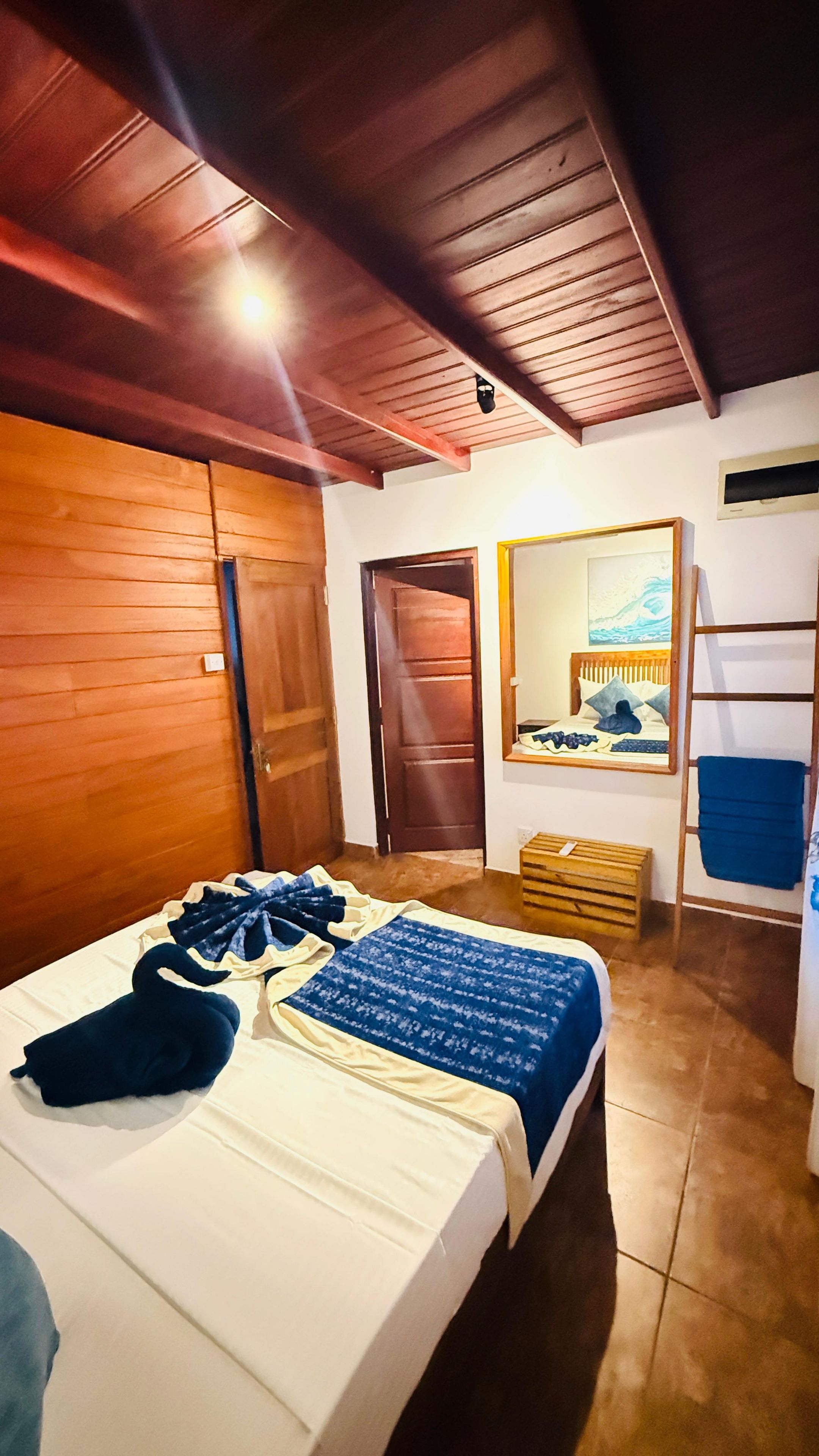 A room with a bed, wooden walls, a door, a mirror, and a window.