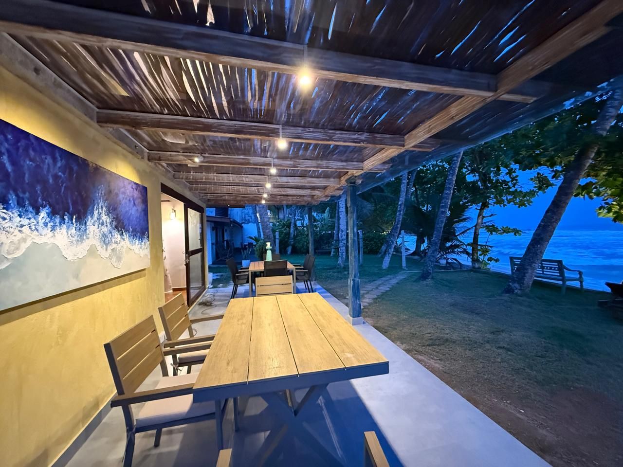 An outdoor dining area with a wooden table and chairs, a mural on the wall, and a view of the ocean.