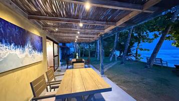 An outdoor dining area with a wooden table and chairs, a mural on the wall, and a view of the ocean.