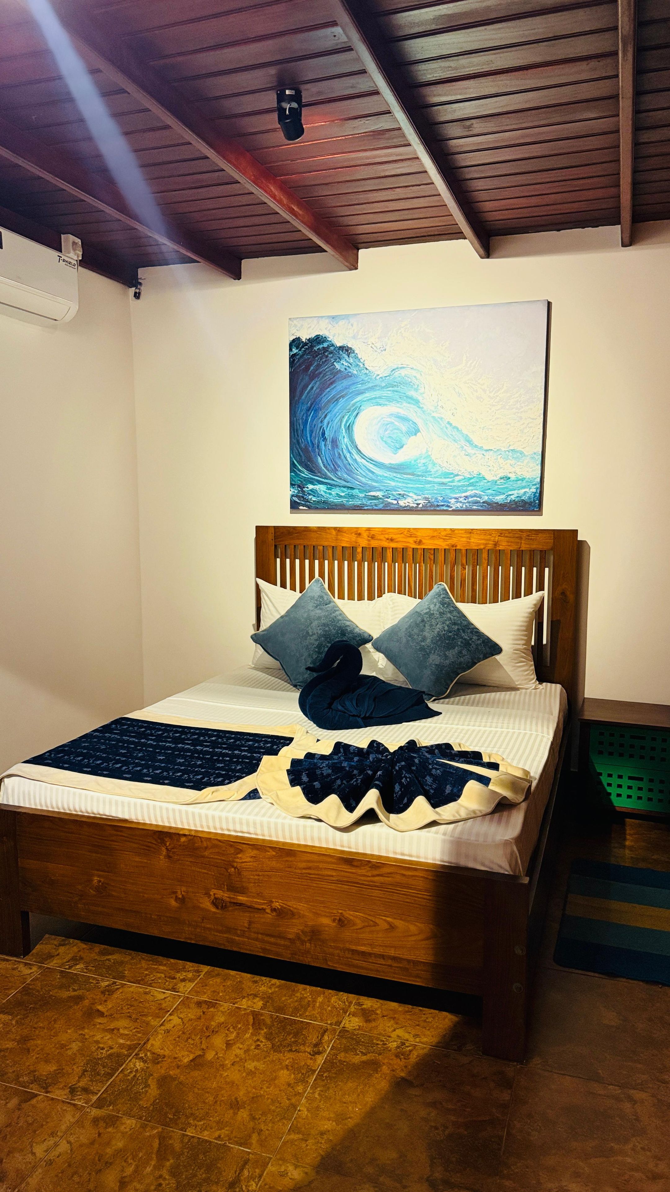 A bed with a wooden headboard, a blue and white abstract painting above it, and a patterned bedspread.