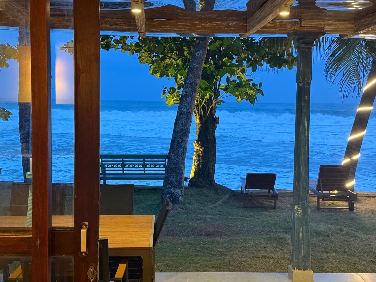 An outdoor seating area with a view of the ocean, wooden pergola, and two lounge chairs.