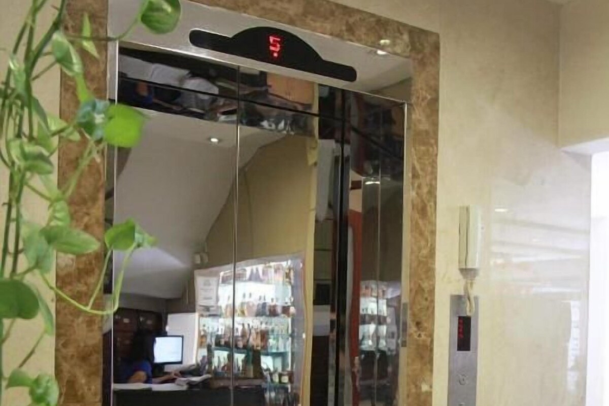 A modern elevator with a digital display, a marble wall, and a plant on the left.