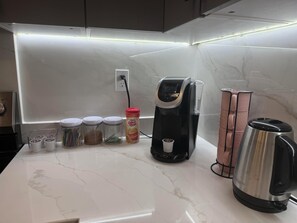 A kitchen counter with a coffee maker, a kettle, and containers of coffee grounds.