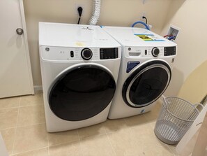 Two front-loading washing machines in a laundry room with a tiled floor and a metal laundry basket.