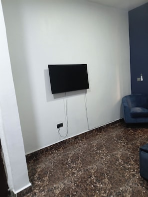 Habitació amb televisió de pantalla plana penjada a la paret, un sofà de color fosc i un sòl amb dibuix de marbre.