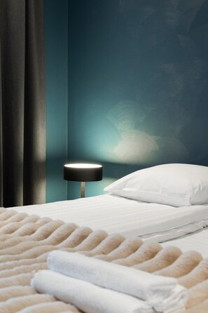Un lit bien fait, avec du linge de lit blanc et une couverture blanche moelleuse, une lampe de chevet et un mur de couleur turquoise.