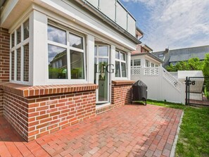Ein Wohnhaus mit Ziegelaußenwand, großen Fenstern und einer gepflasterten Terrasse.
