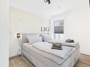 Ein Schlafzimmer mit einem Bett, Kissen, einer Wandleuchte und einem Fenster.