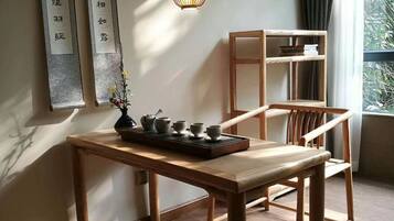 Una habitació amb taula de fusta, llum penjant, prestatges i finestra amb cortines.