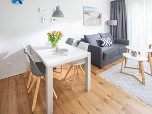 A modern living room with a white dining table, grey sofa, and a small round table. - 2 Meerzeit Norderney (Norderney)