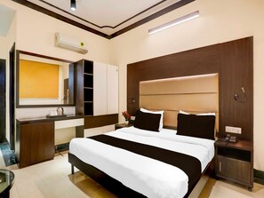 A hotel room with a large bed, a bedside table with a phone, a mirror, a wardrobe, and a small table with a vase. - Collection O Sushant Lok Phase 1 (Gurugram)