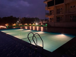 A swimming pool with a metal railing, surrounded by a building with multiple floors and balconies. - Sansav Garden Resort (Mangalore)