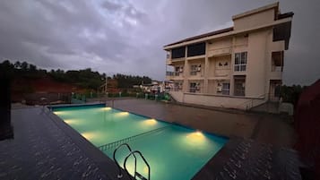 Una piscina con una escalera de metal, rodeada por un edificio de varios pisos y balcones.