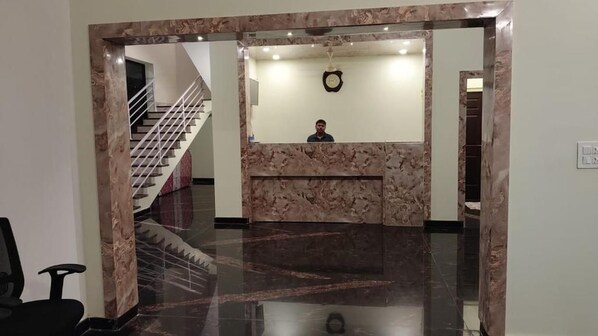 A reception area with a marble reception desk, a clock on the wall, and a staircase in the background.