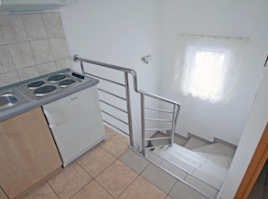 A kitchen with a stove, sink, and a metal railing leading to a staircase. - Beachfront Apartment With 1 Bedroom (Posedarje)