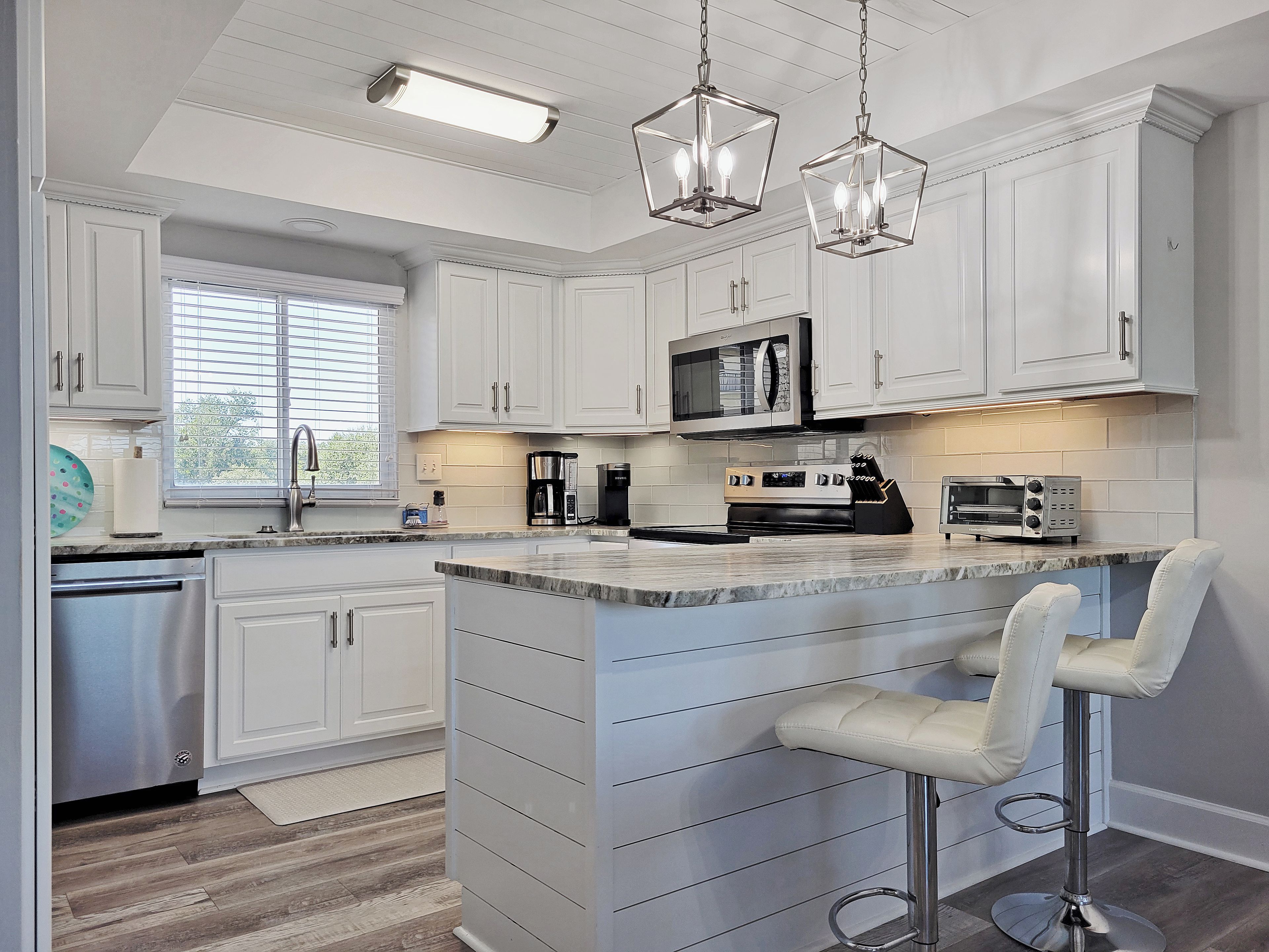 A modern kitchen with white cabinetry, a central island with bar stools, stainless steel appliances, and pendant lighting.
