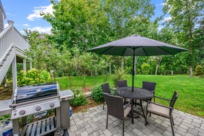 Eine Terrasse im Freien mit einem Grill, einem Tisch mit Stühlen und einem großen Sonnenschirm.