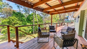 A covered outdoor deck with wooden railings, a metal railing, and several chairs. - Two Decks on Bass | A Simple Blue Mountains Escape (Wentworth Falls)