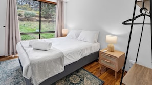 A bedroom with a bed, bedside table, lamp, and a view of the outdoors. - Two Decks on Bass | A Simple Blue Mountains Escape (Wentworth Falls)
