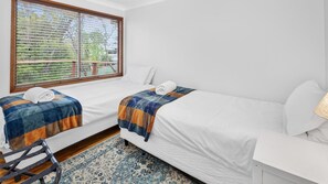 Habitación de hotel con dos camas, una ventana con persianas, una mesita y una silla.