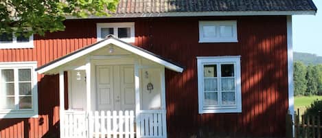 A red wooden house with a white porch and a small front yard.