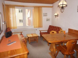 A dining area with a wooden table and chairs, a sofa, and a window with curtains. - Paradies 026 Appartement/Fewo, Bad, WC, 4-Bettwohnung 4-Bettwohnung by Interhome (Arosa)