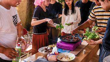 A group of people around a table with food, a portable stove, and a grill.