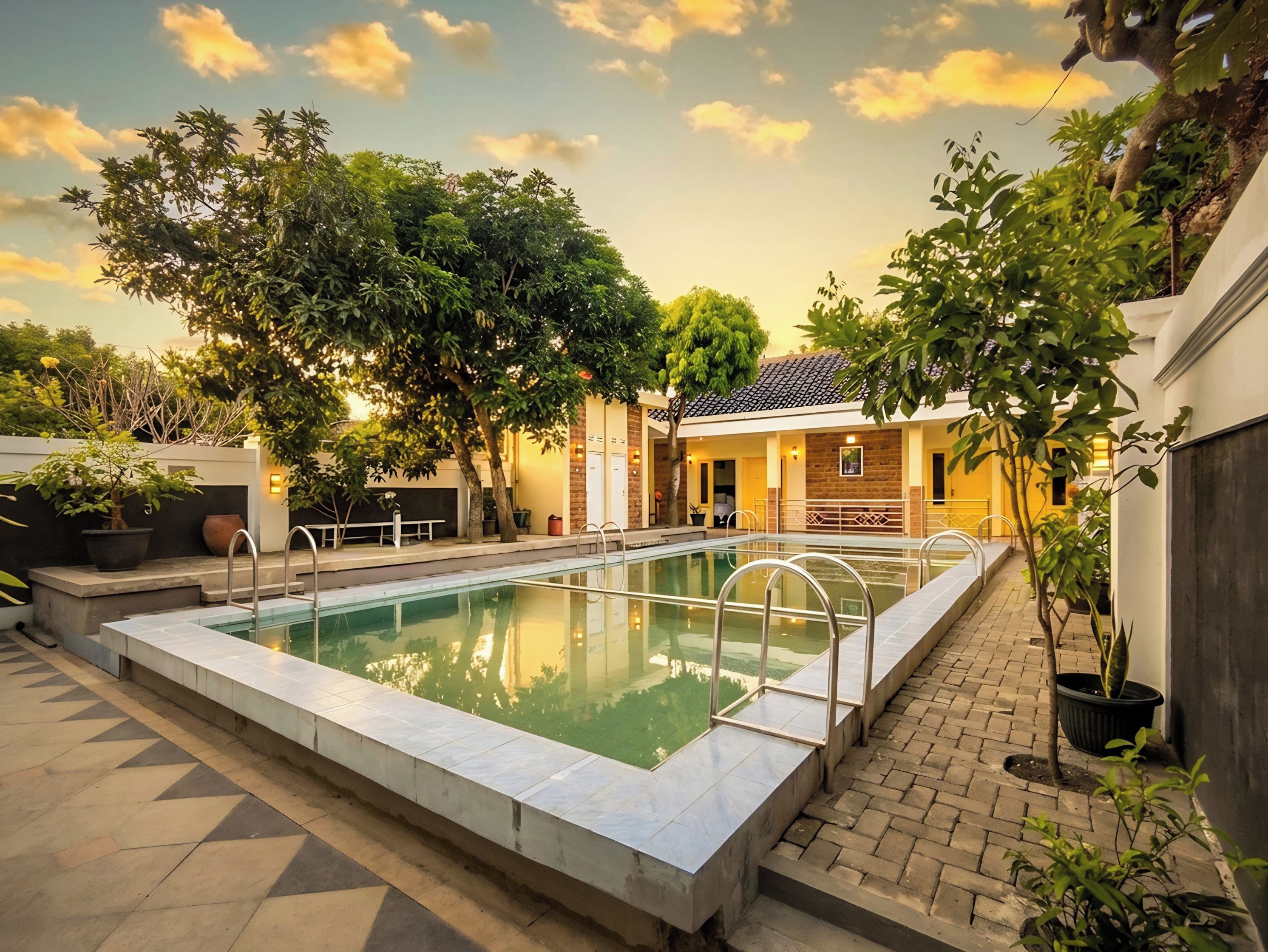 A rectangular swimming pool with metal railings, surrounded by a paved walkway and potted plants.